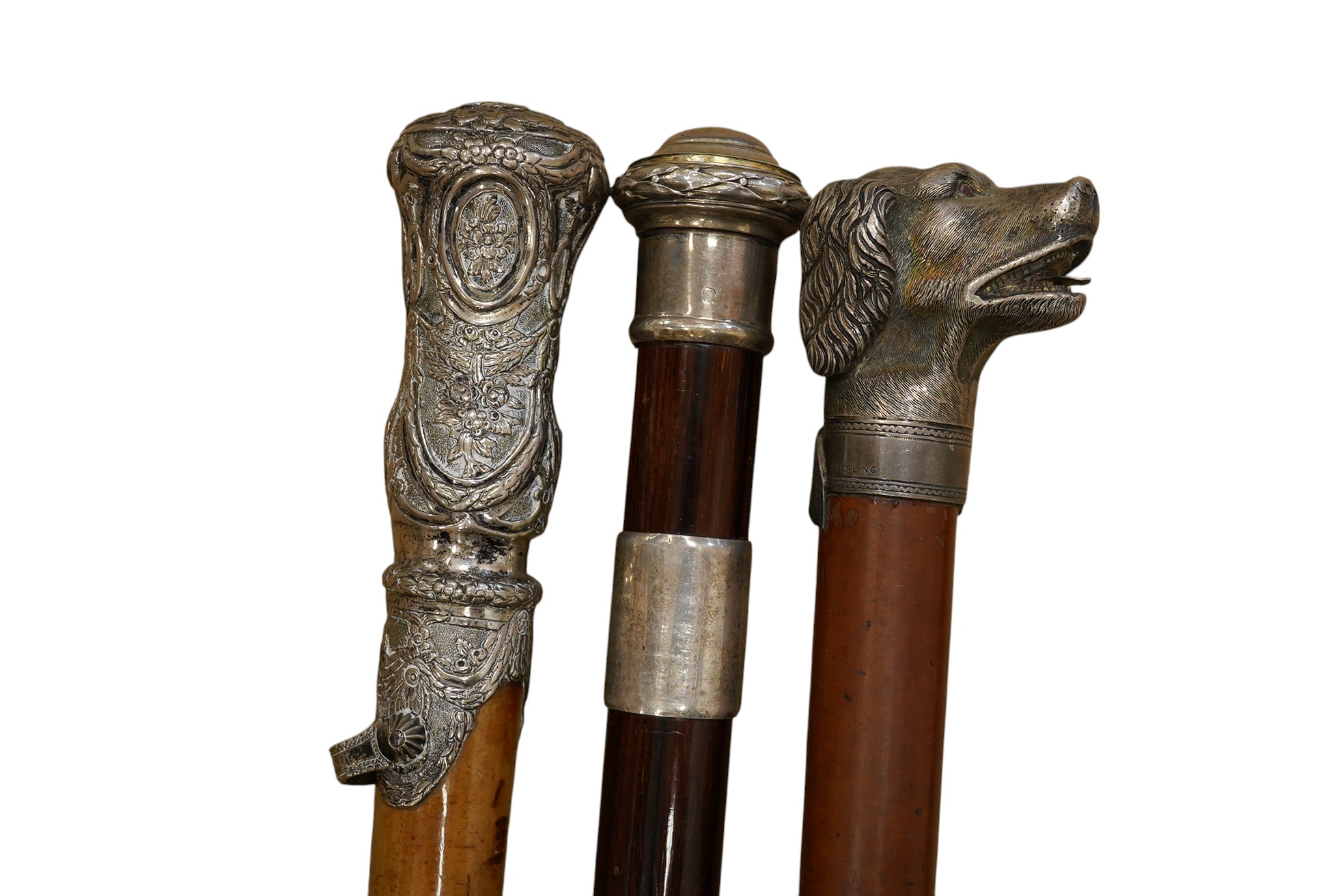 Three 19th century walking sticks, two with silver tops to include a dogs head example, one with unmarked embossed white metal top, largest 97cm in length